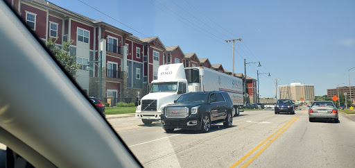 A black SUV waiting behind a large truck on a busy city street, with residential buildings in the background.