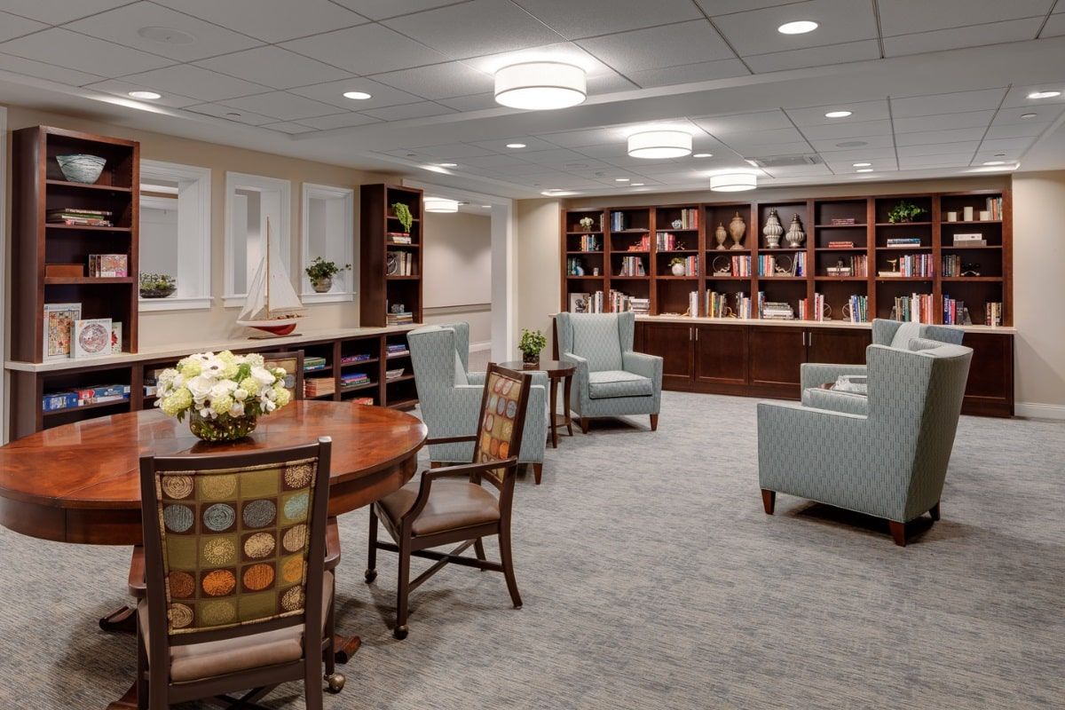 A cozy interior space featuring a seating area with armchairs, bookshelves filled with books, and a central table.