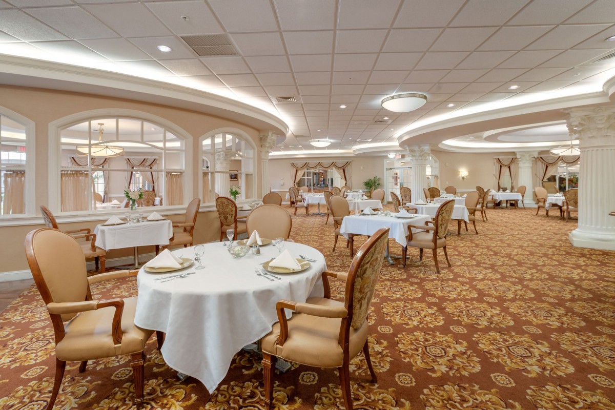 An elegant dining room with neatly arranged tables and chairs, ornate chandeliers, and a carpeted floor.