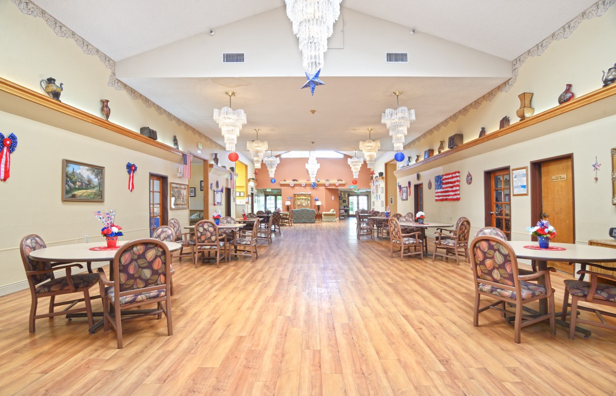 A spacious hall with chandeliers, wood flooring, and arranged tables and chairs.