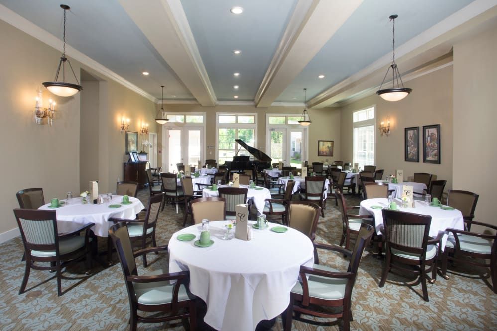 An elegant dining room with tables set for a meal and a piano in the background.
