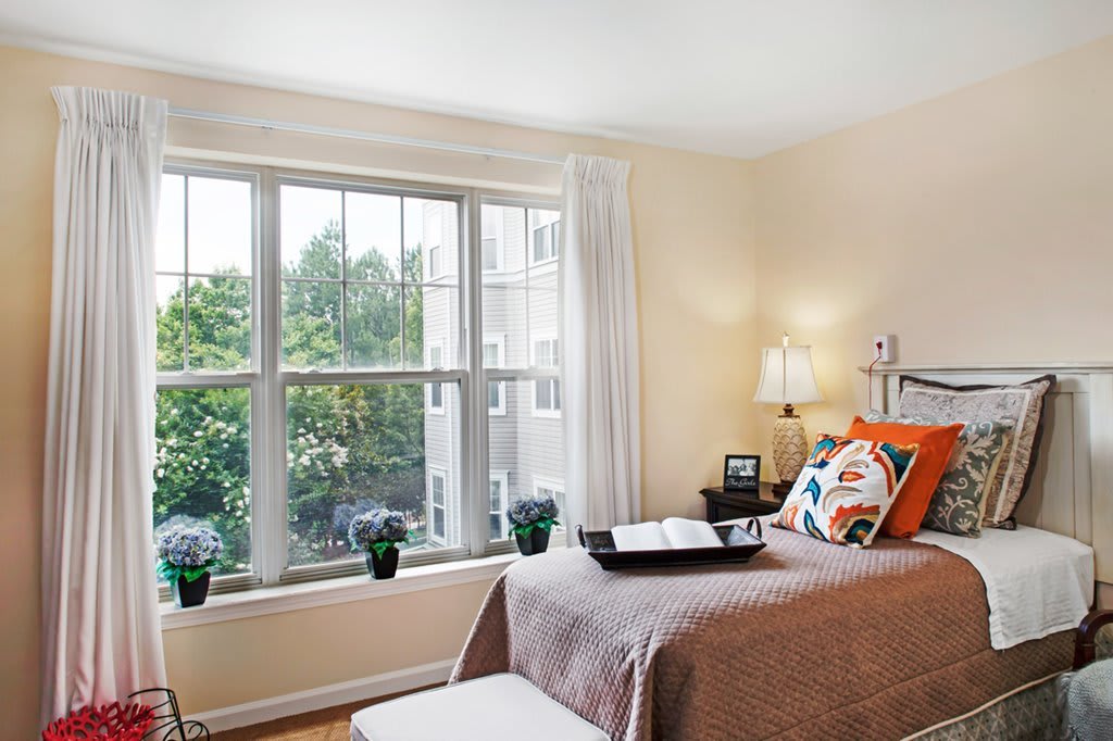 A cozy bedroom with a large window letting in natural light, decorated with plants and colorful pillows.
