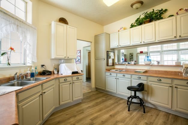A clean and organized kitchen with white cabinets, a countertop, and a stool.