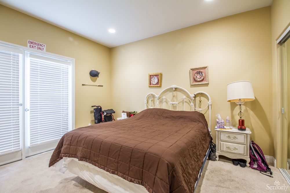 A cozy bedroom featuring a neatly made bed with brown bedding, flanked by nightstands and a lamp, with artwork adorning the walls.