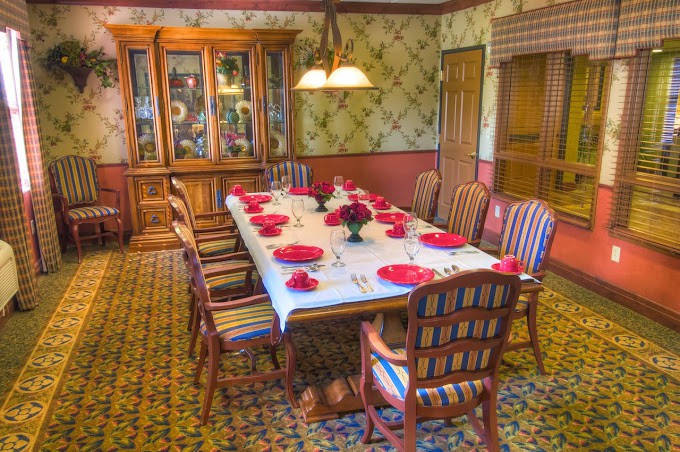 A cozy dining room with a table set for a meal, featuring wooden chairs, a china cabinet, and a warm chandelier.