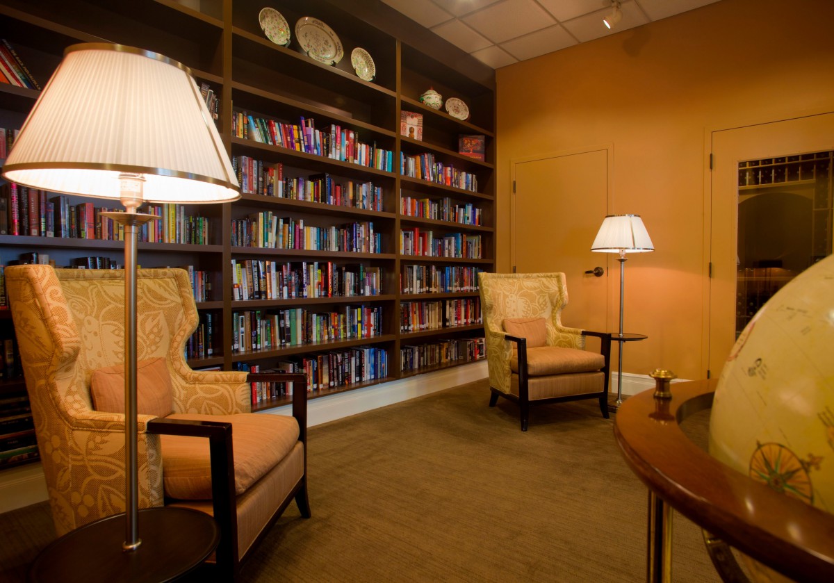A cozy library room with bookshelves, armchairs, and lamps for reading.