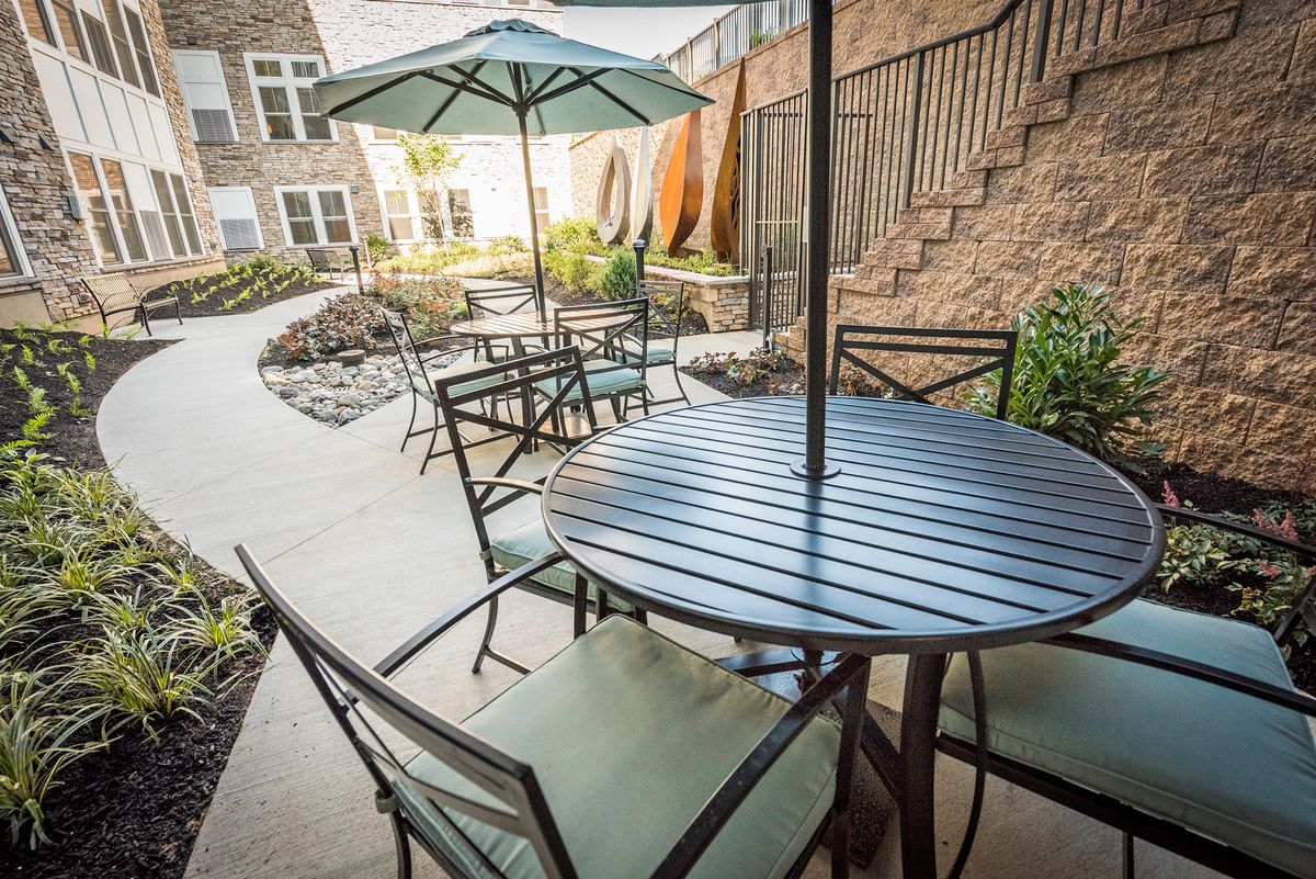 A cozy outdoor patio area featuring tables with umbrellas and chairs, set in a well-maintained garden.