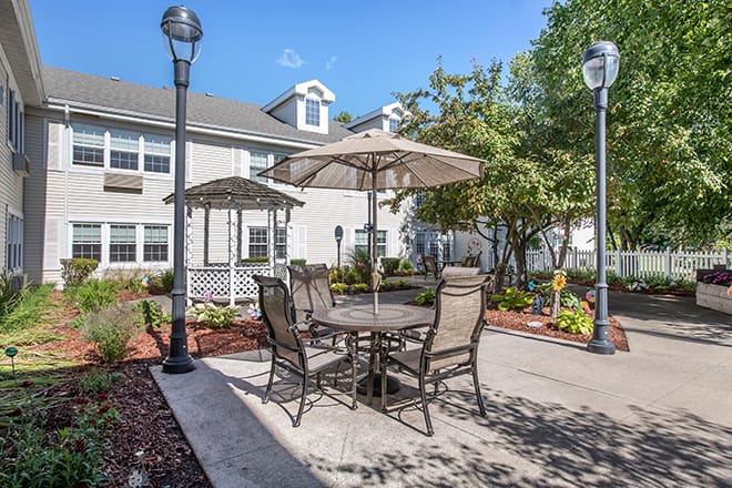 A cozy outdoor patio area with tables and chairs under umbrellas, surrounded by a well-maintained garden in a residential setting.