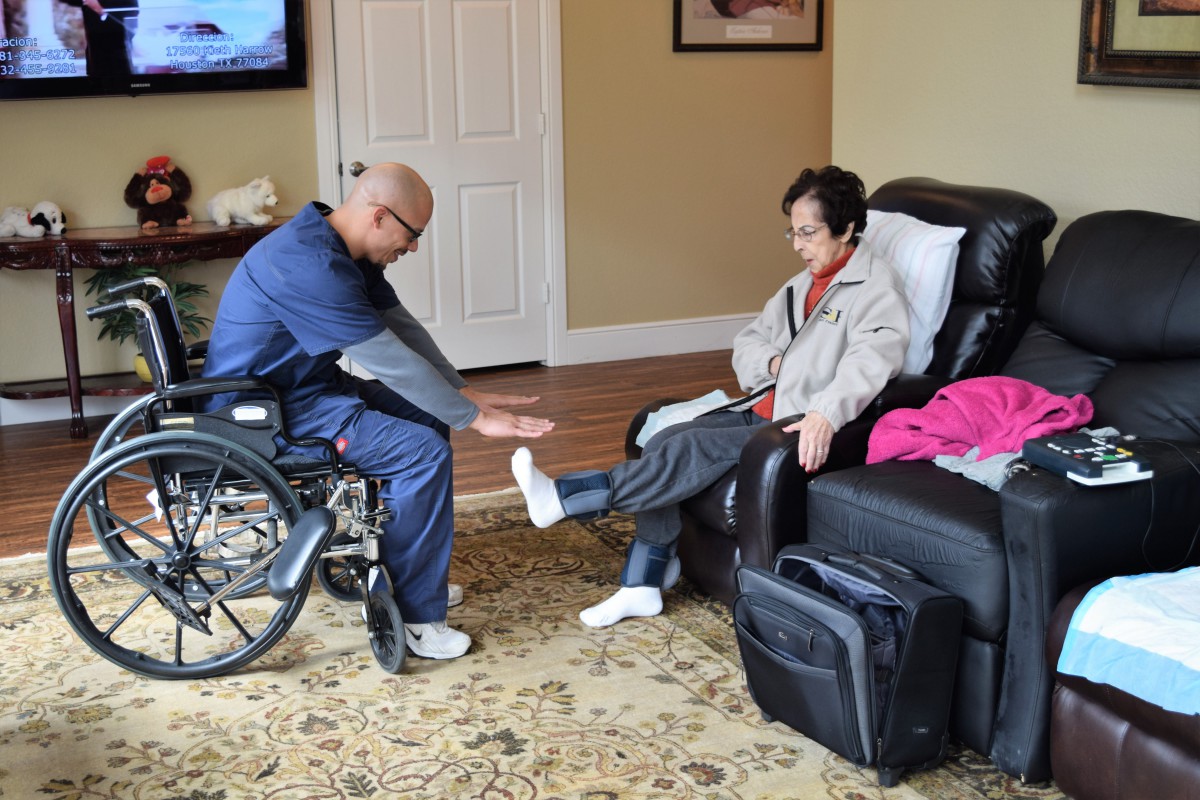 A caregiver assists a person with leg exercises in a home setting.