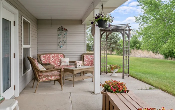 A cozy patio area with wicker chairs and floral cushions, overlooking a lush garden.