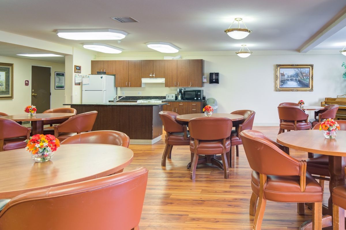 A well-lit kitchen and dining area with multiple tables and chairs, featuring a hardwood floor.