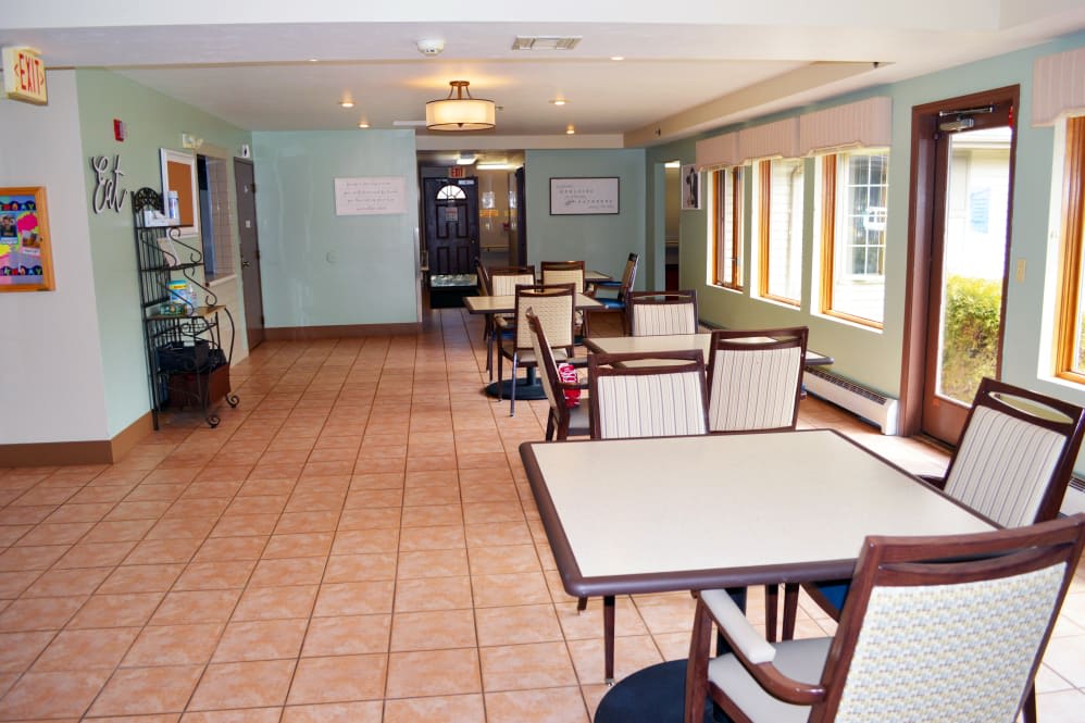 An empty dining area with tables and chairs, featuring large windows and a tile floor.