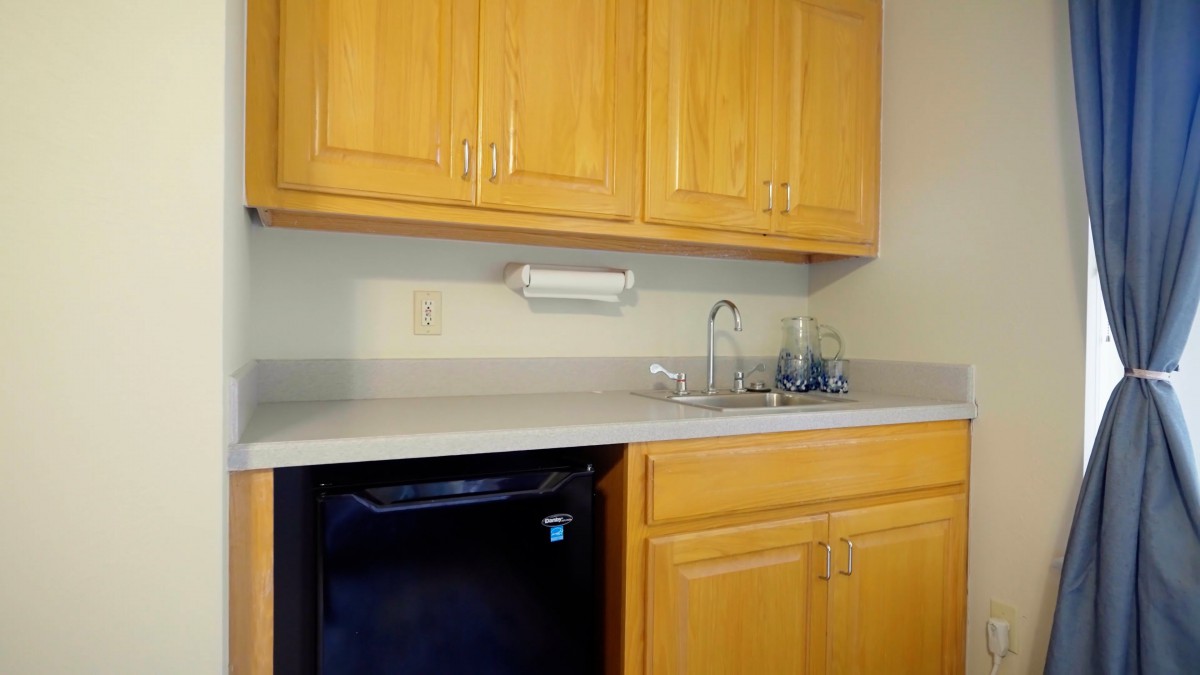 A small kitchen area featuring wooden cabinets, a countertop with a sink, and a mini fridge.
