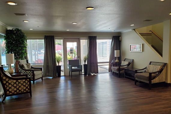 A modern living room with wooden flooring, large windows with curtains, and comfortable chairs.