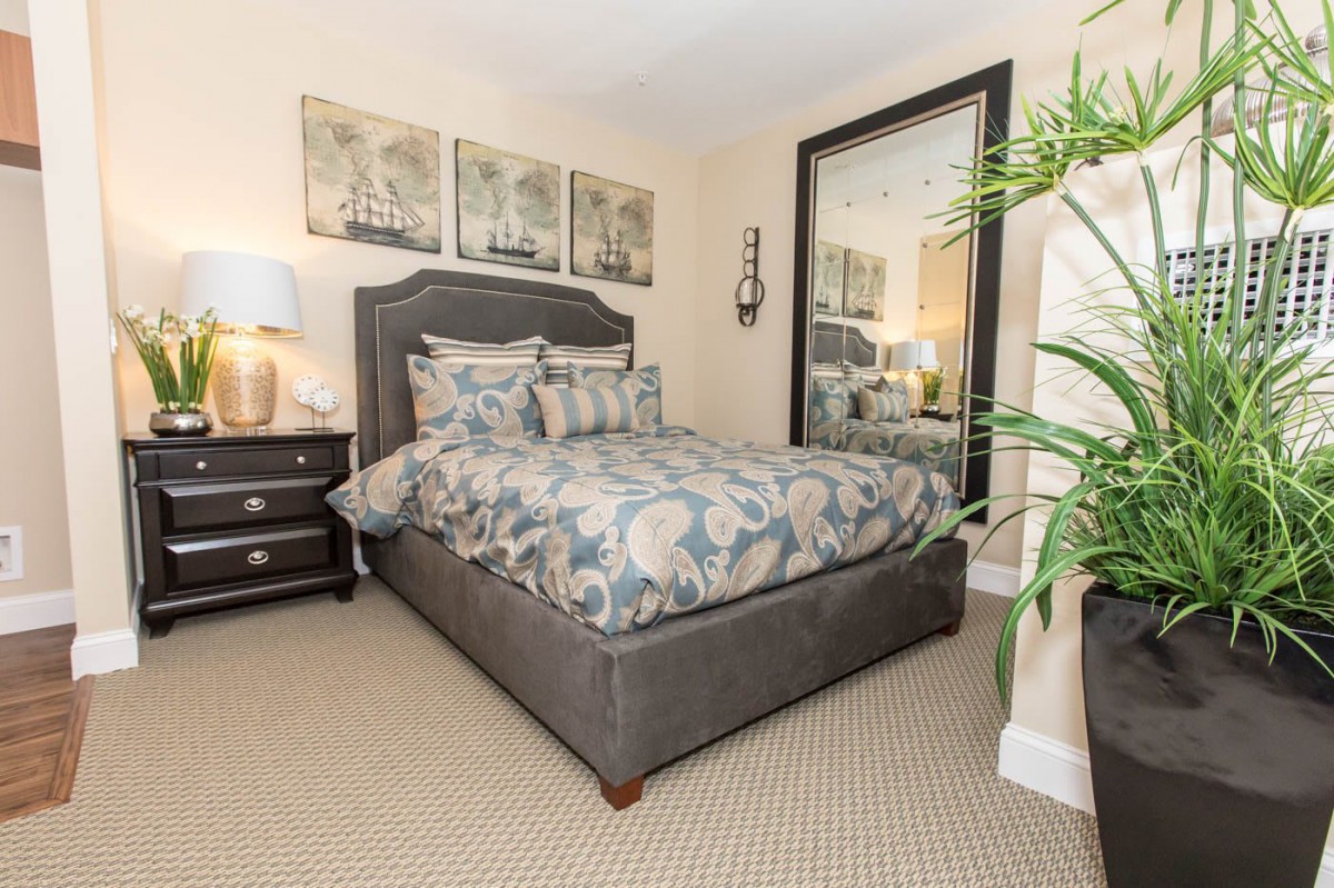 A cozy and elegantly decorated bedroom featuring a plush bed, large mirror, bedside lamp, and indoor plant.