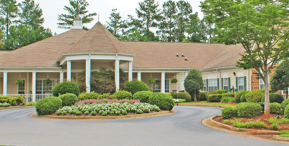 A large house with a circular driveway surrounded by well-maintained landscaping, including trees, shrubs, and flowers.