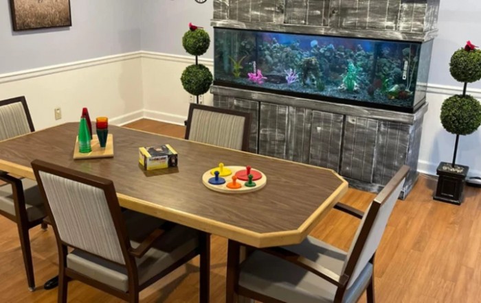 A cozy dining room with a wooden table, chairs, and an aquarium in the background.