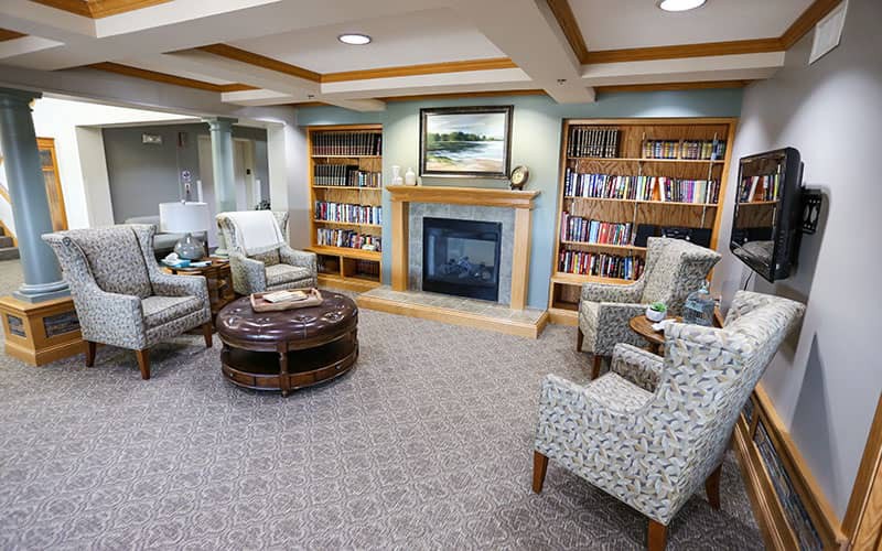 A cozy library room with a fireplace, bookshelves, and comfortable seating.