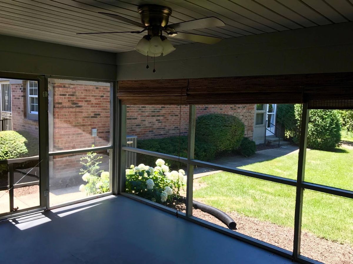 A sunroom with large windows offering a view of the garden and brick exterior, featuring an overhead fan.