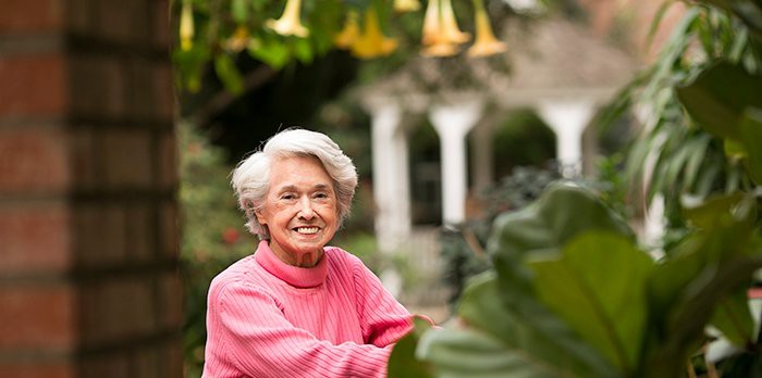 An elderly woman in a pink sweater enjoying her time in a lush garden.