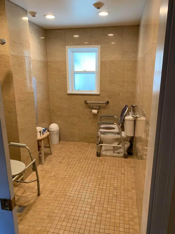 An accessible bathroom featuring grab bars, a chair, and a window.