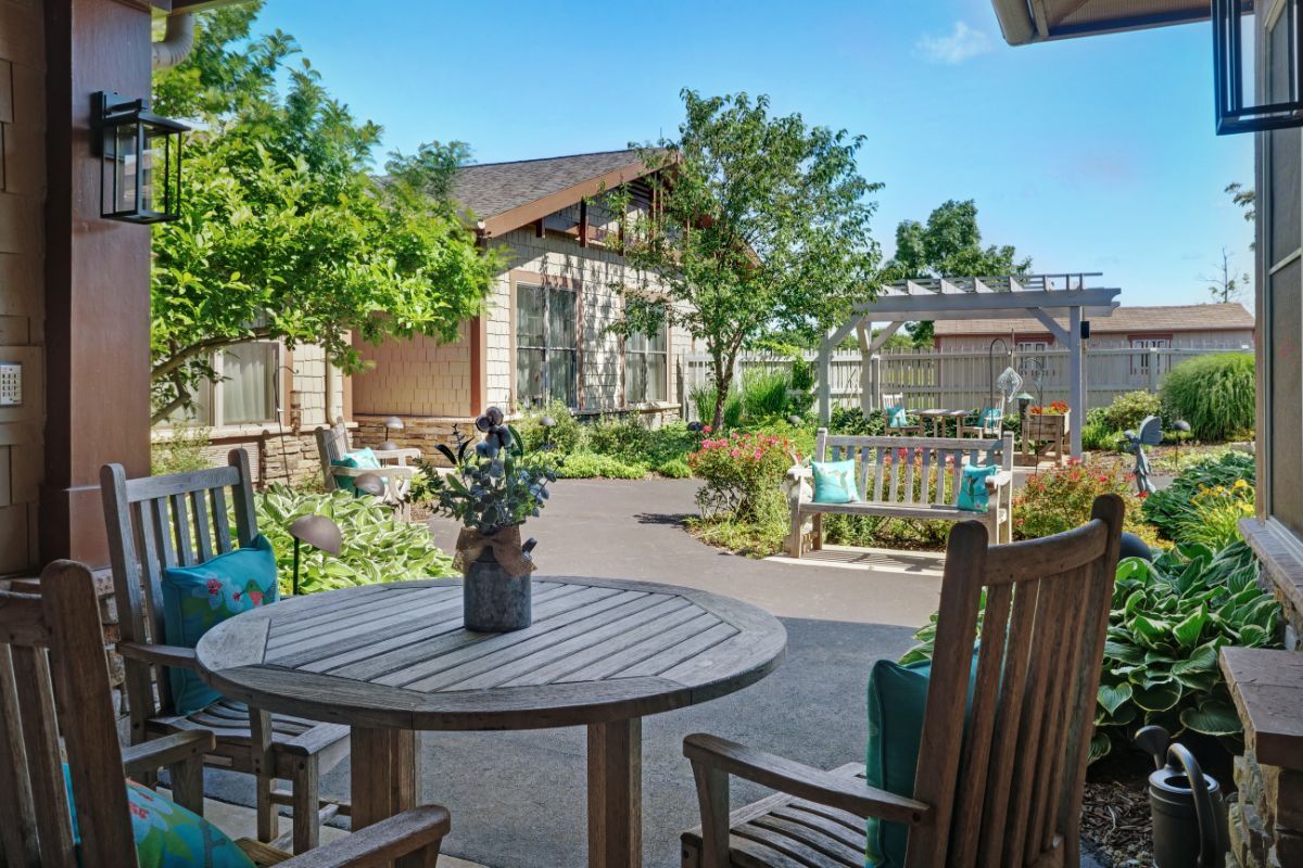 A tranquil outdoor patio surrounded by lush greenery, featuring comfortable wooden seating and a sunny atmosphere.