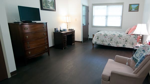 A cozy bedroom with a desk, lamp, dresser, and bed.