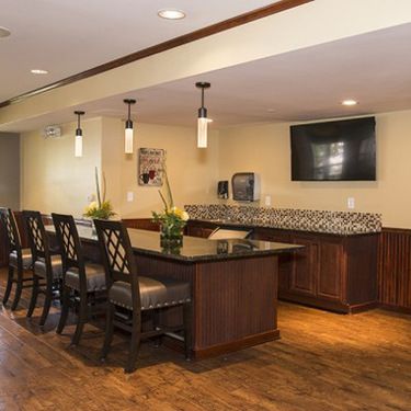 A modern kitchen and bar area with a long counter, chairs, pendant lighting, and a mounted television.