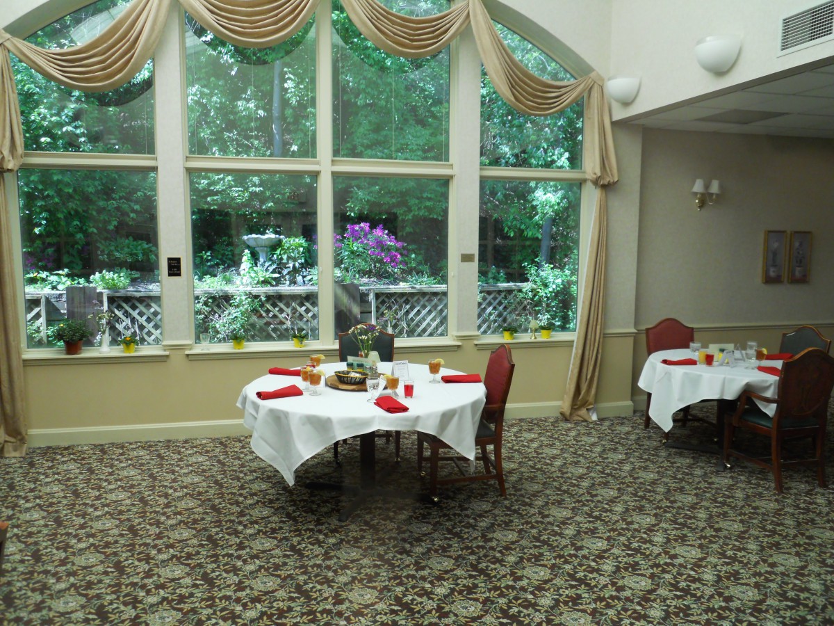 An elegantly decorated dining room with tables set for guests, featuring large windows overlooking a garden.