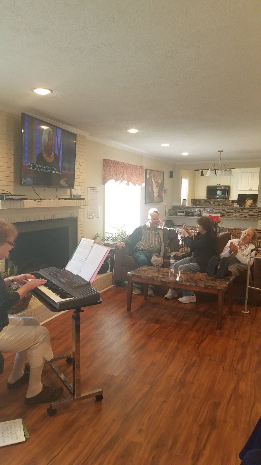 A group of people in a living room, enjoying music played on a piano while seated comfortably.