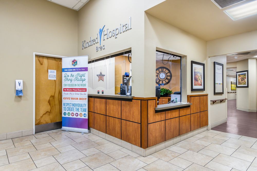 The image shows the reception area of a hospital with a front desk and informational signage.
