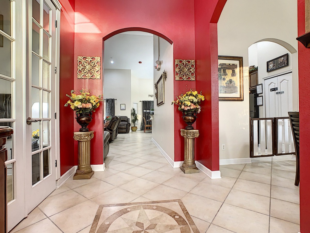 A stylish home entrance featuring vibrant red walls, decorative vases with flowers, and a tiled floor leading into a spacious living area.