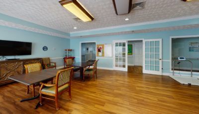 A spacious and well-lit room with wooden floors, featuring chairs, tables, and light blue walls.