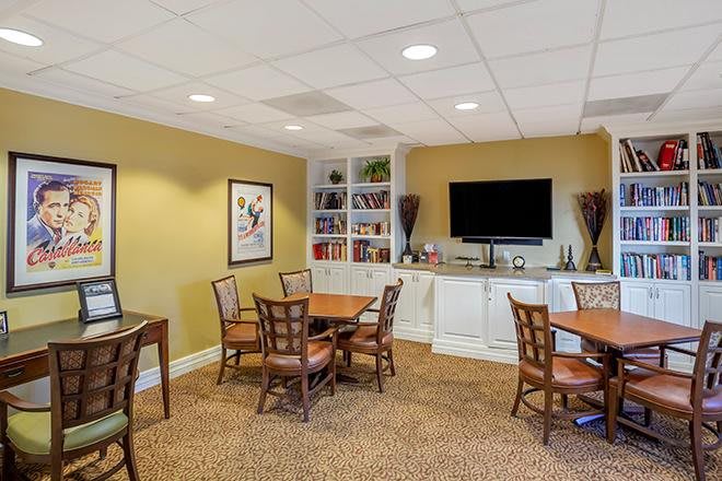 A cozy meeting room with tables, chairs, and a TV, decorated with artwork and bookshelves.