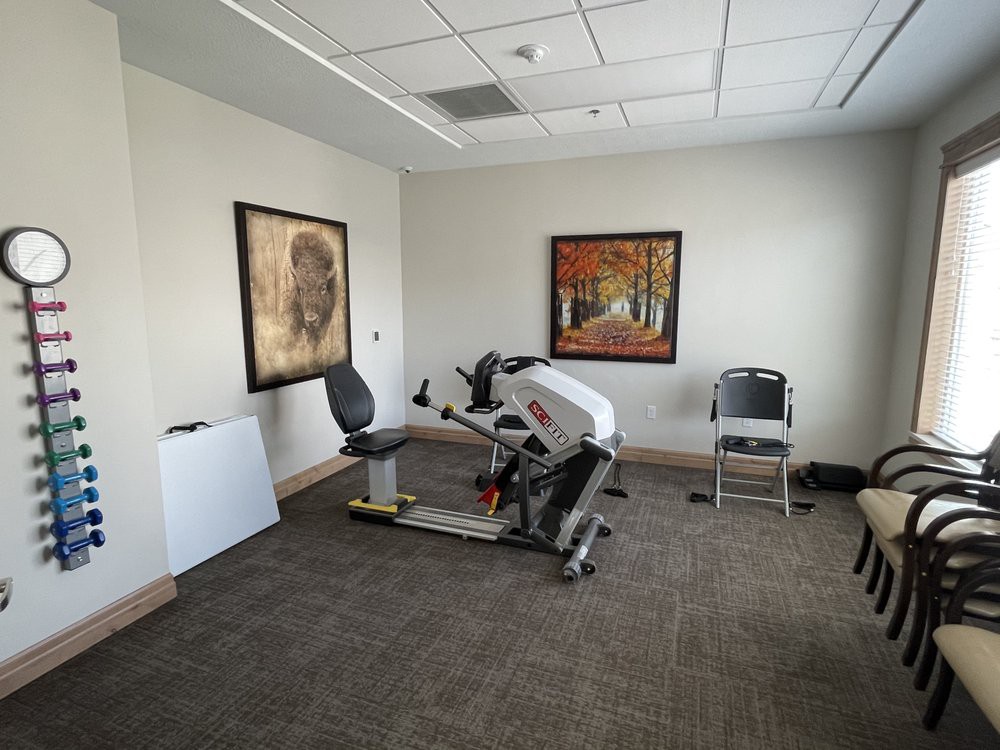 A small exercise room with a stationary bike, chairs, and paintings on the wall.