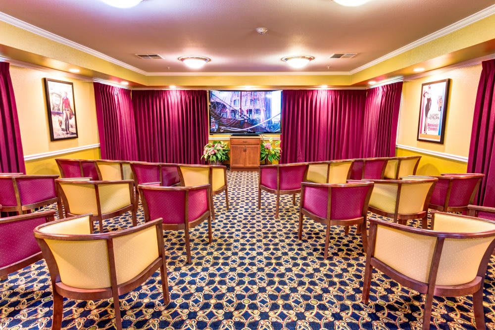 A well-lit room with arranged chairs facing a stage with curtains.