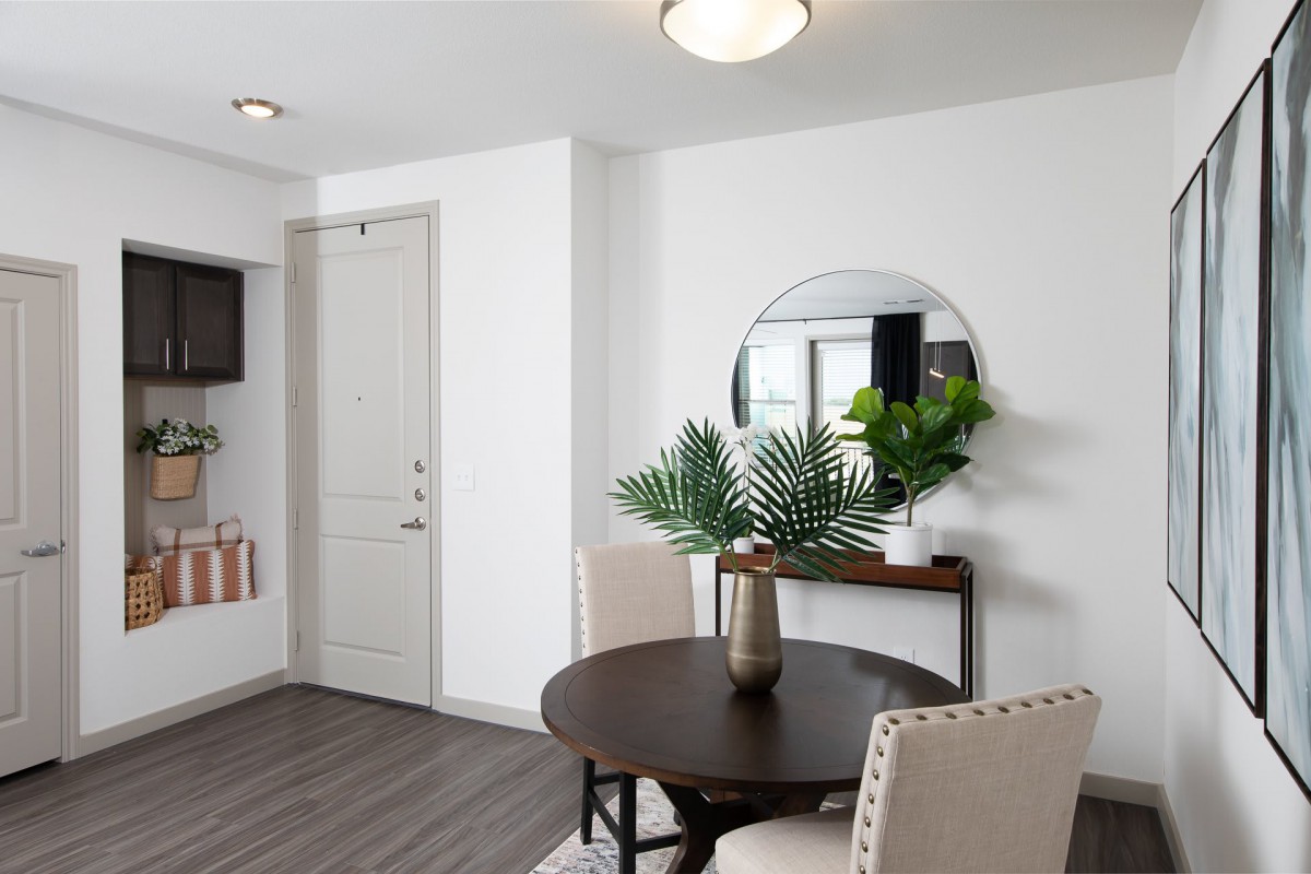 A modern dining area with a round table and upholstered chairs, complemented by a mirror and decorative plants.