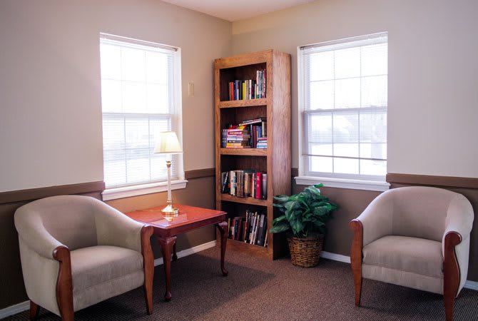 Cozy reading nook with two chairs, a wooden bookshelf, and a small table with a lamp.