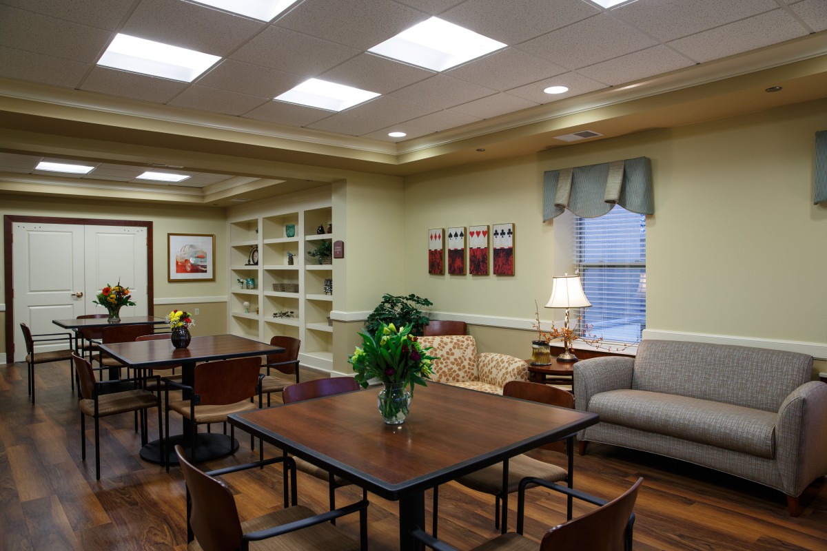 A cozy library reading room with tables, chairs, and bookshelves.