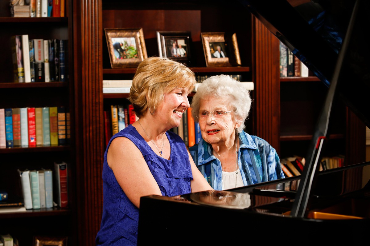Two women enjoying a conversation at the piano in a cozy library setting.
