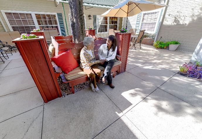 Two people sitting and talking on a patio with an umbrella.