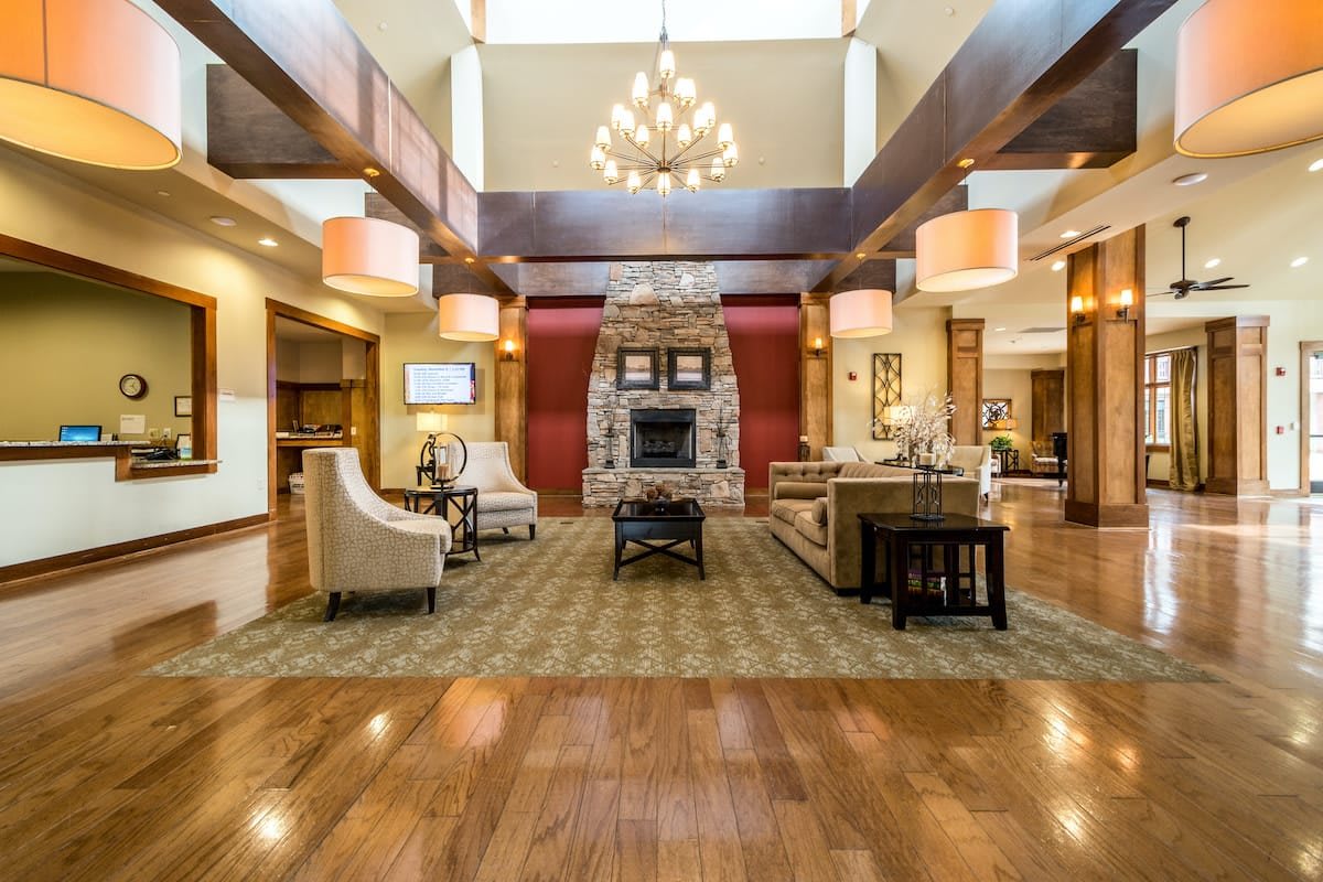 A spacious and elegantly designed lobby featuring a stone fireplace, comfortable seating, a large chandelier, and wood flooring.