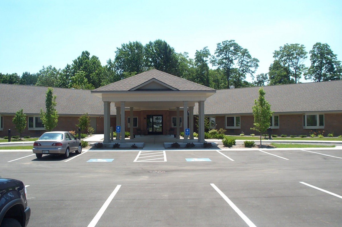 Image of a building with a covered entrance, featuring columns and an adjacent parking lot.