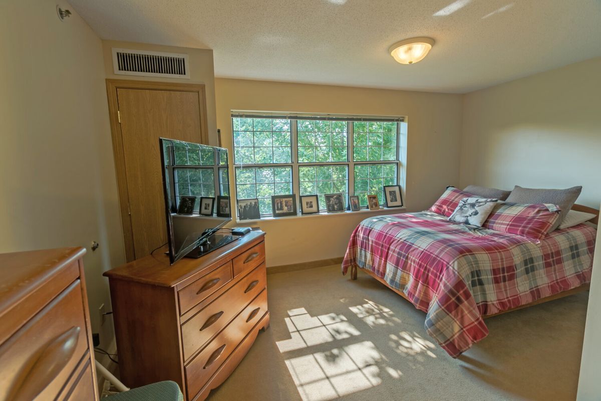 A cozy bedroom with a large window, bed, dresser, and television.