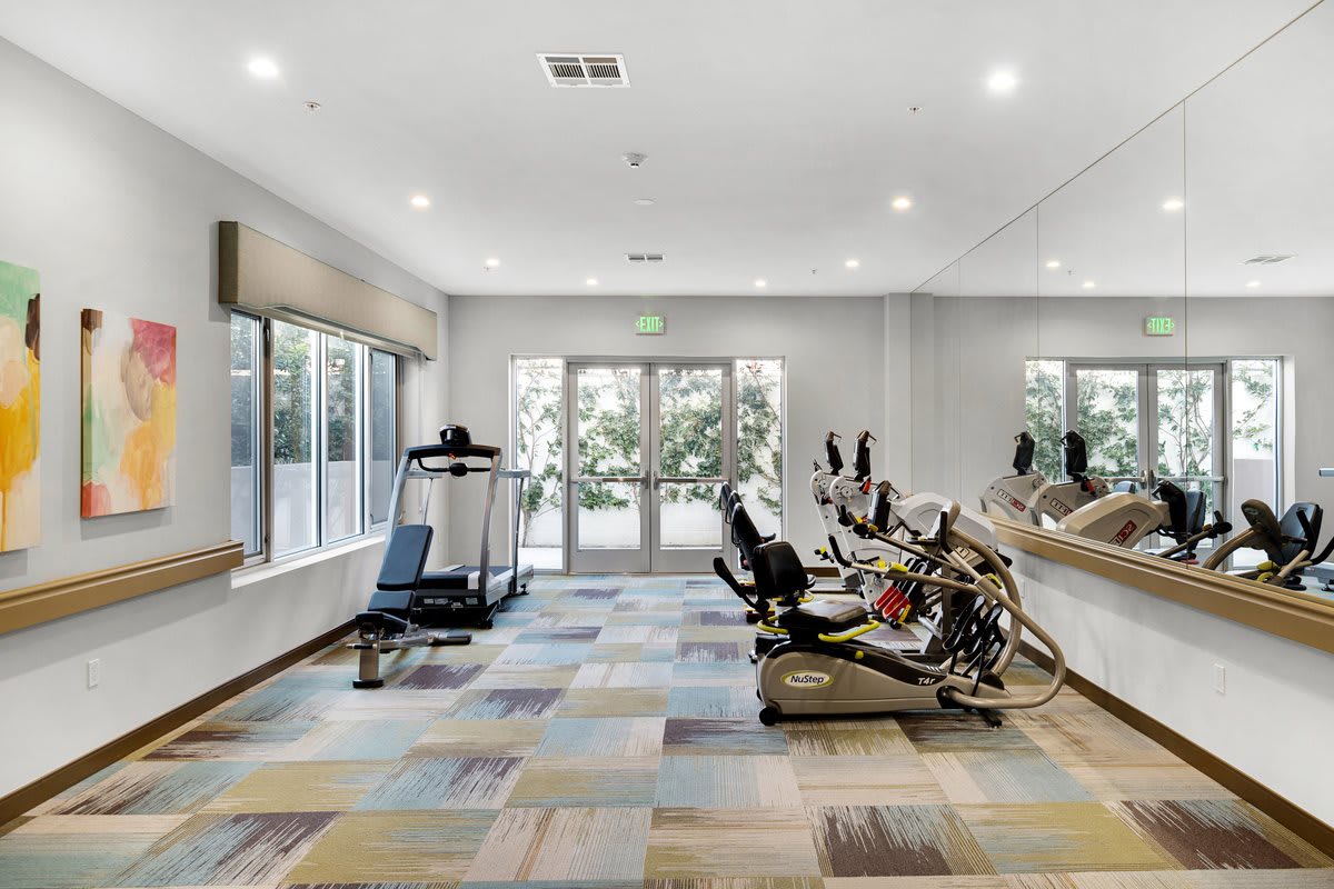 A modern gym with exercise equipment including a treadmill and stationary bikes, brightly lit by natural light.