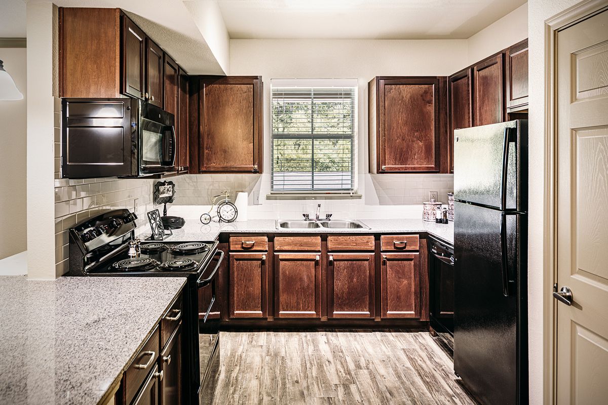 A modern kitchen with wooden cabinets and black appliances, featuring a window above the sink.