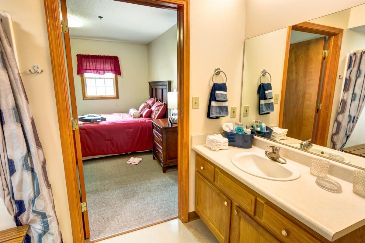 A cozy bedroom and bathroom setup with wooden furniture and a large mirror.