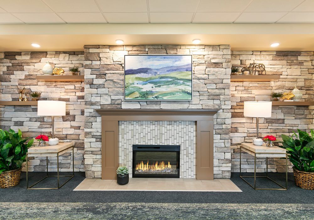A cozy living room with a stone fireplace, adorned with artwork and flanked by stylish lamps.
