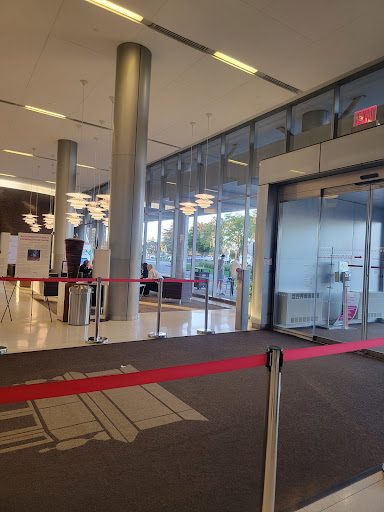 A modern lobby with glass doors and a waiting area, featuring red rope barriers.