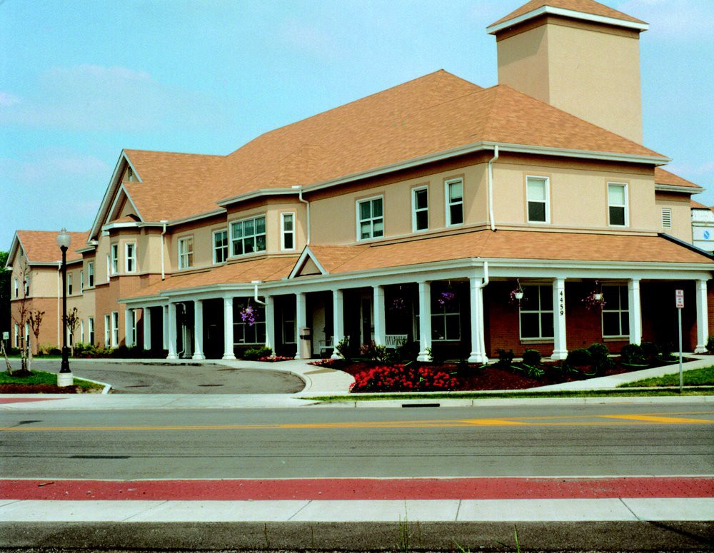 A two-story residential building with columns and a red roof, seen from across the street.